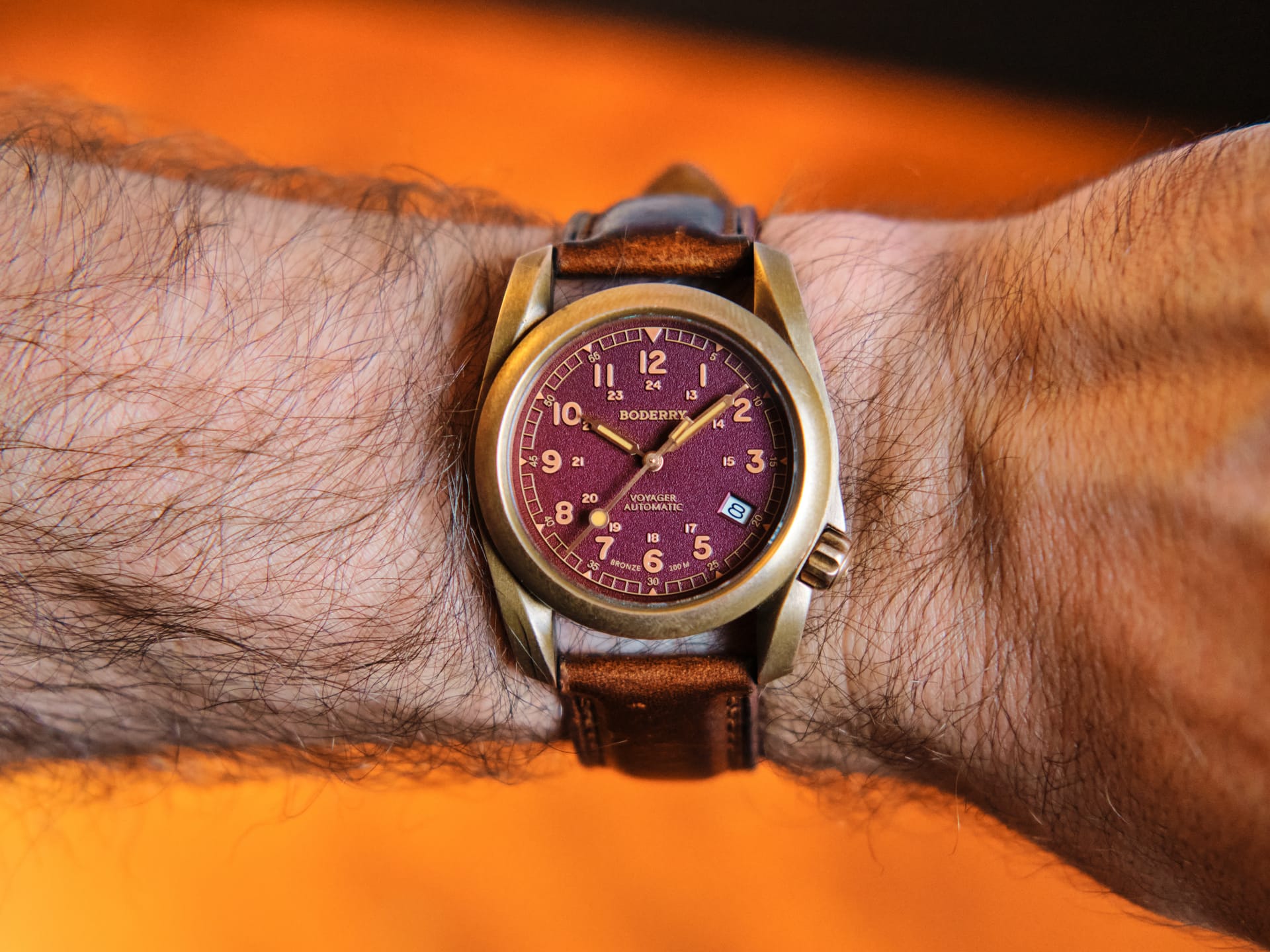 A watch with a burgundy dial and a bronze case, worn on a wrist