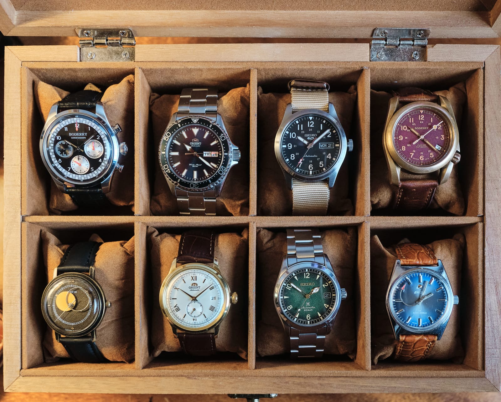 Eight watches in an open wooden watch box, among them a burgundy dial and a blue one